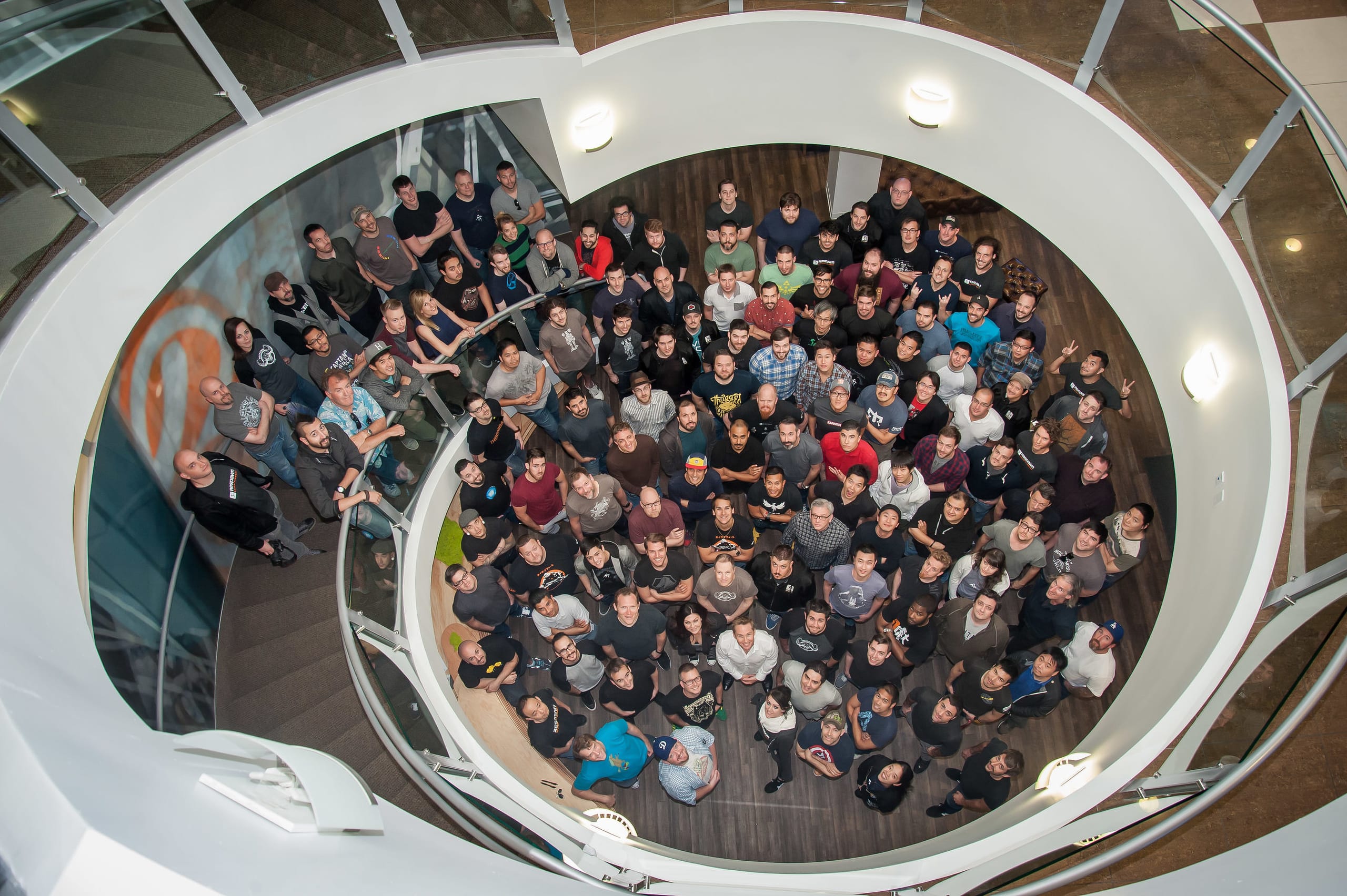 Overhead photograph of roughly two hundred employees gathered on a floor below and looking up through a circular atrium opening at a company all-hands