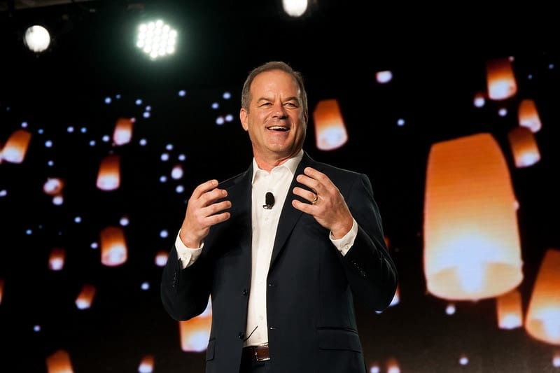 An executive giving a keynote in front of a stage backdrop of glowing lanterns