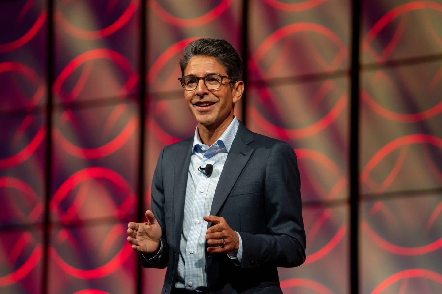 A corporate executive presenting on stage against a red LED backdrop at a conference keynote