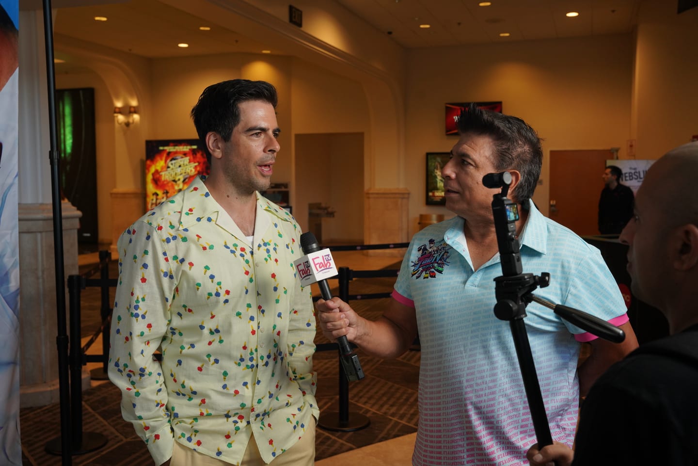 Eli Roth speaking into a handheld press microphone during an interview in the AMC Americana at Brand lobby