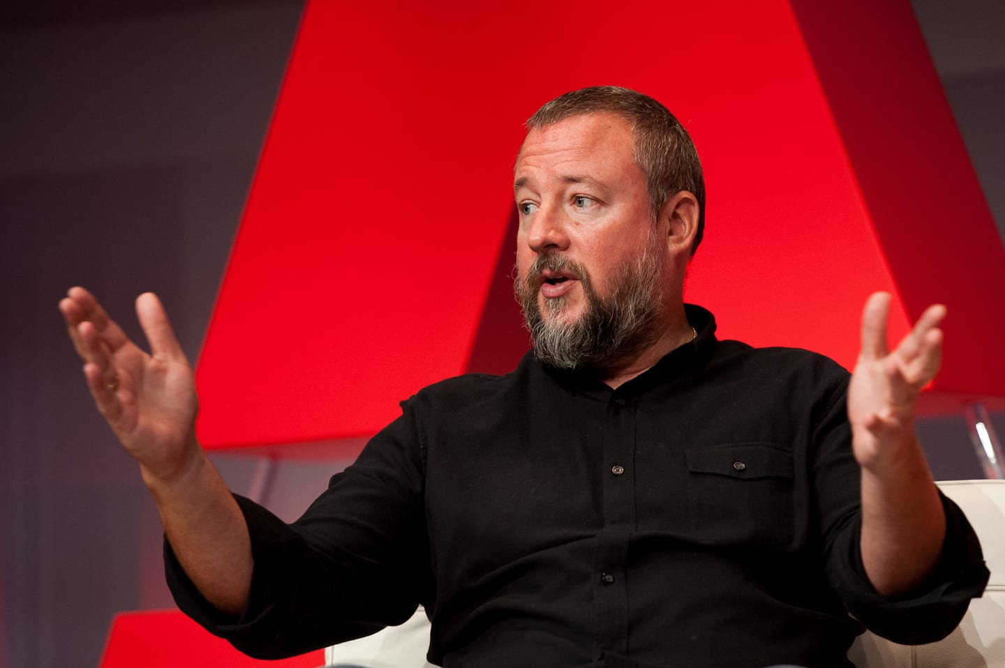 Executive speaking animatedly during a fireside chat against a red stage backdrop