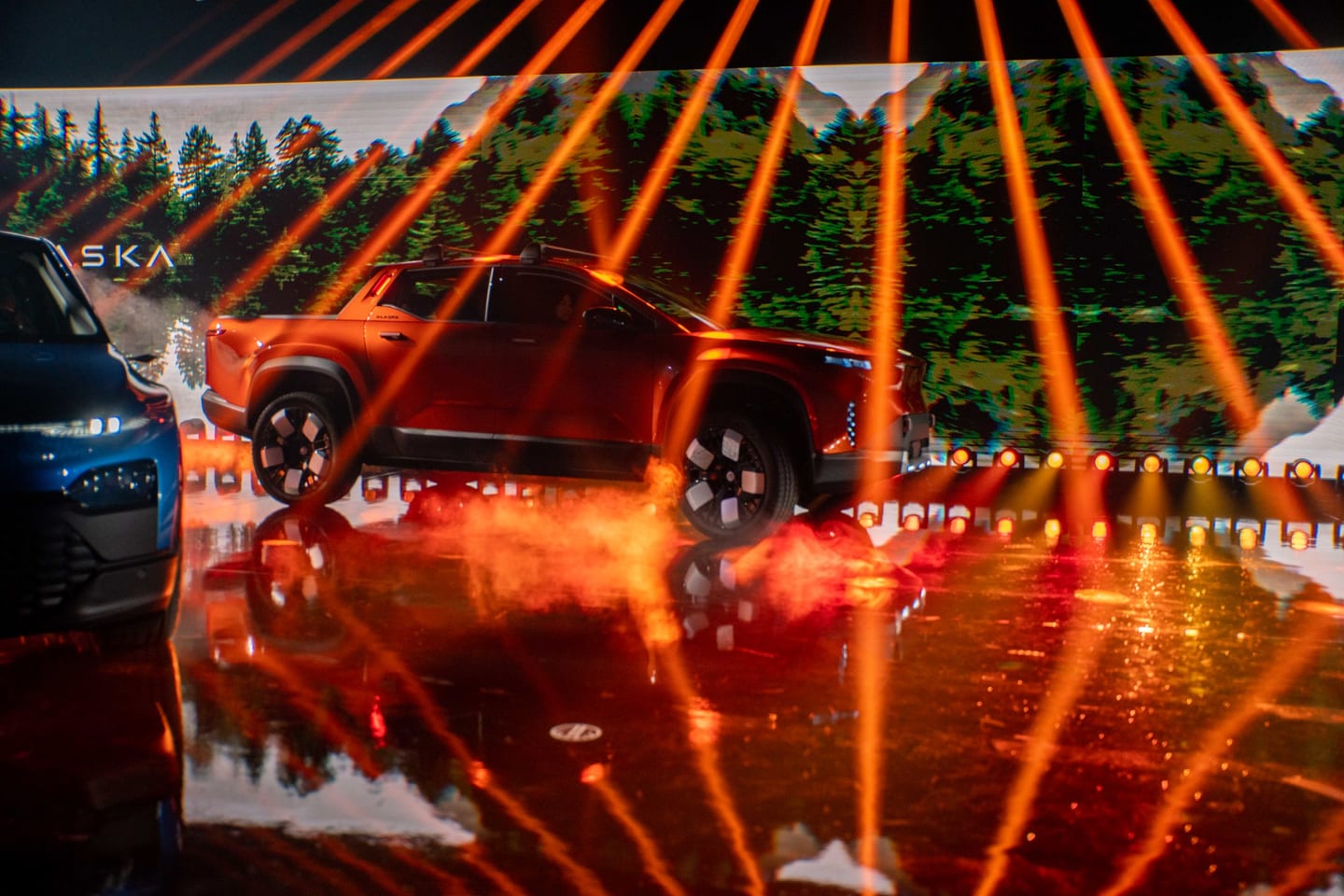 The orange Fisker Alaska on the wet reveal stage under orange beams