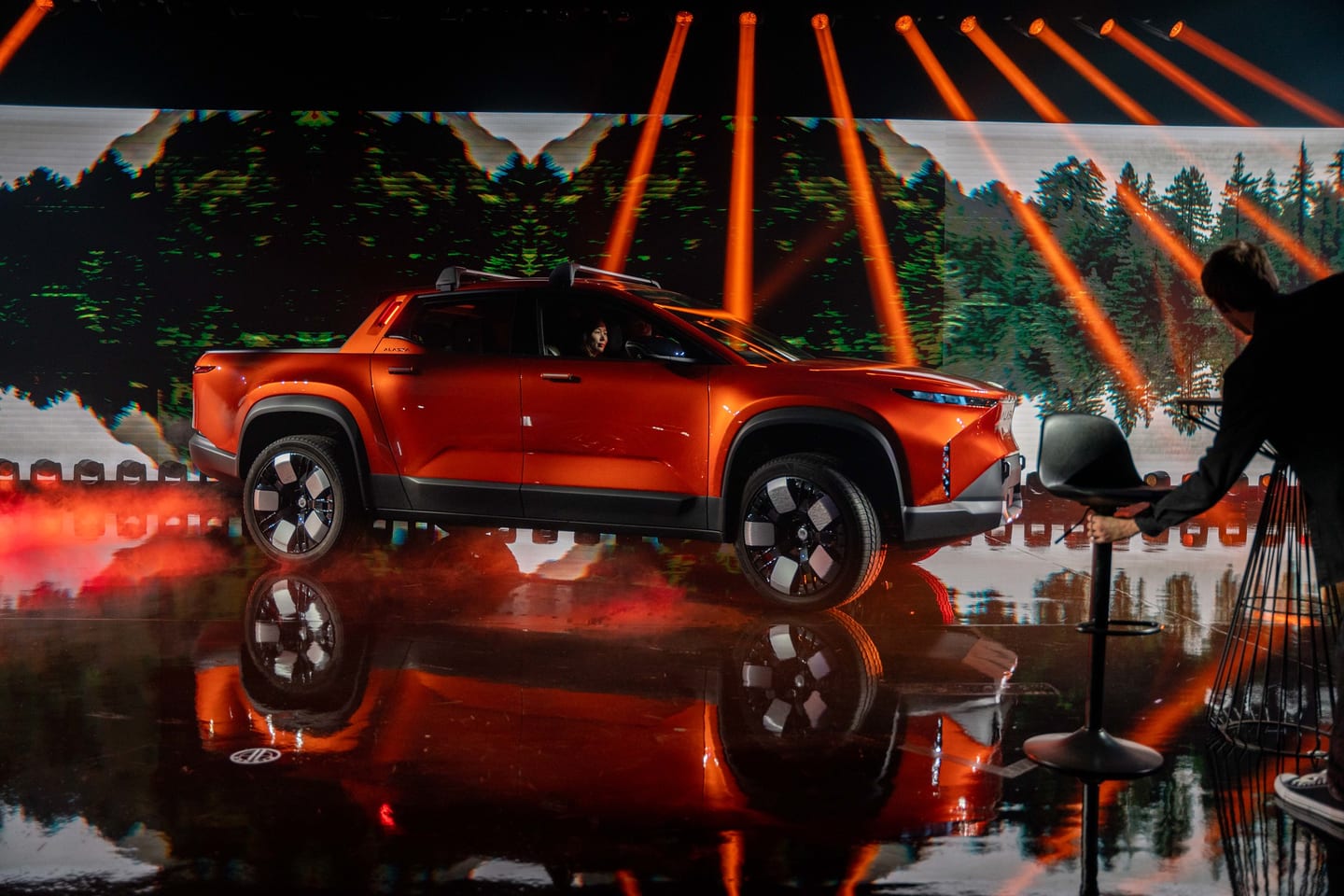 The orange Fisker Alaska pickup on stage against a forest screen under light beams