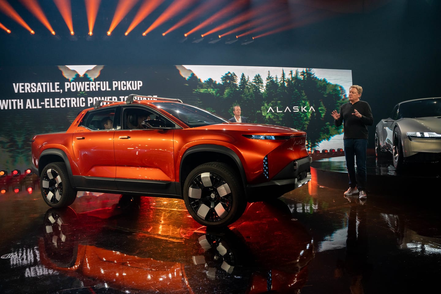 A presenter beside the orange Fisker Alaska on stage