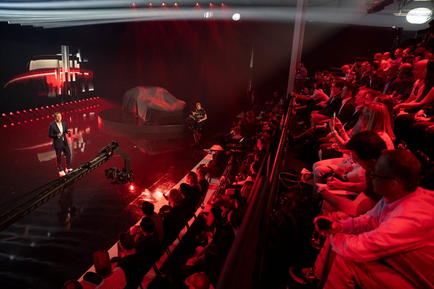 The audience in red light with a covered vehicle on the stage