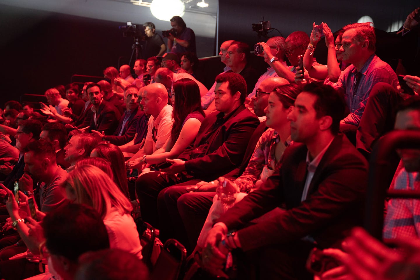 The audience seated in deep red stage light
