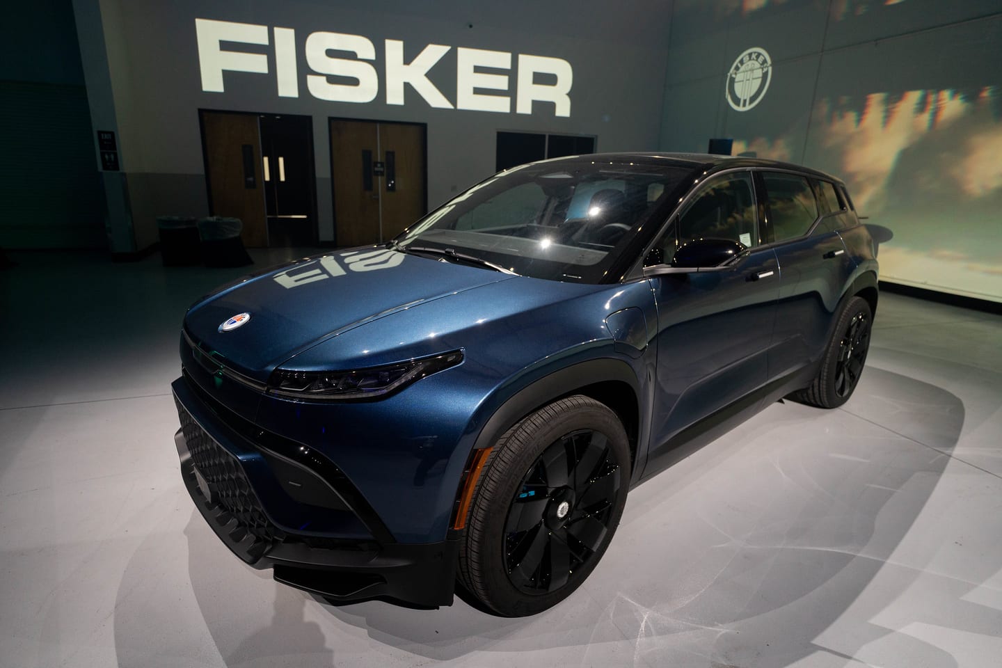 A dark blue Fisker Ocean parked beneath the FISKER sign