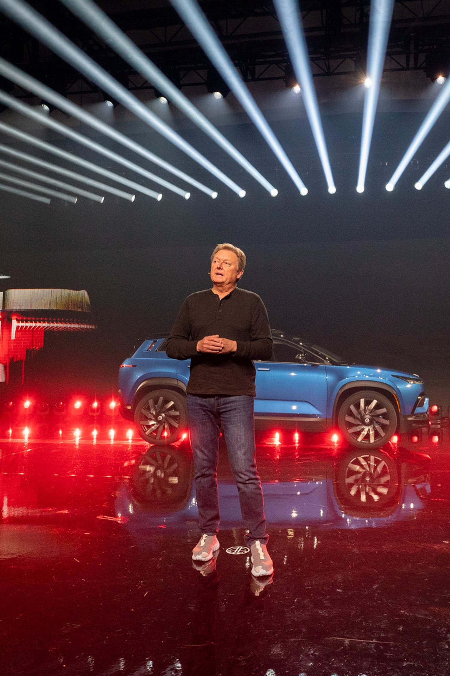 A presenter standing beside a blue Fisker SUV under red floor lights