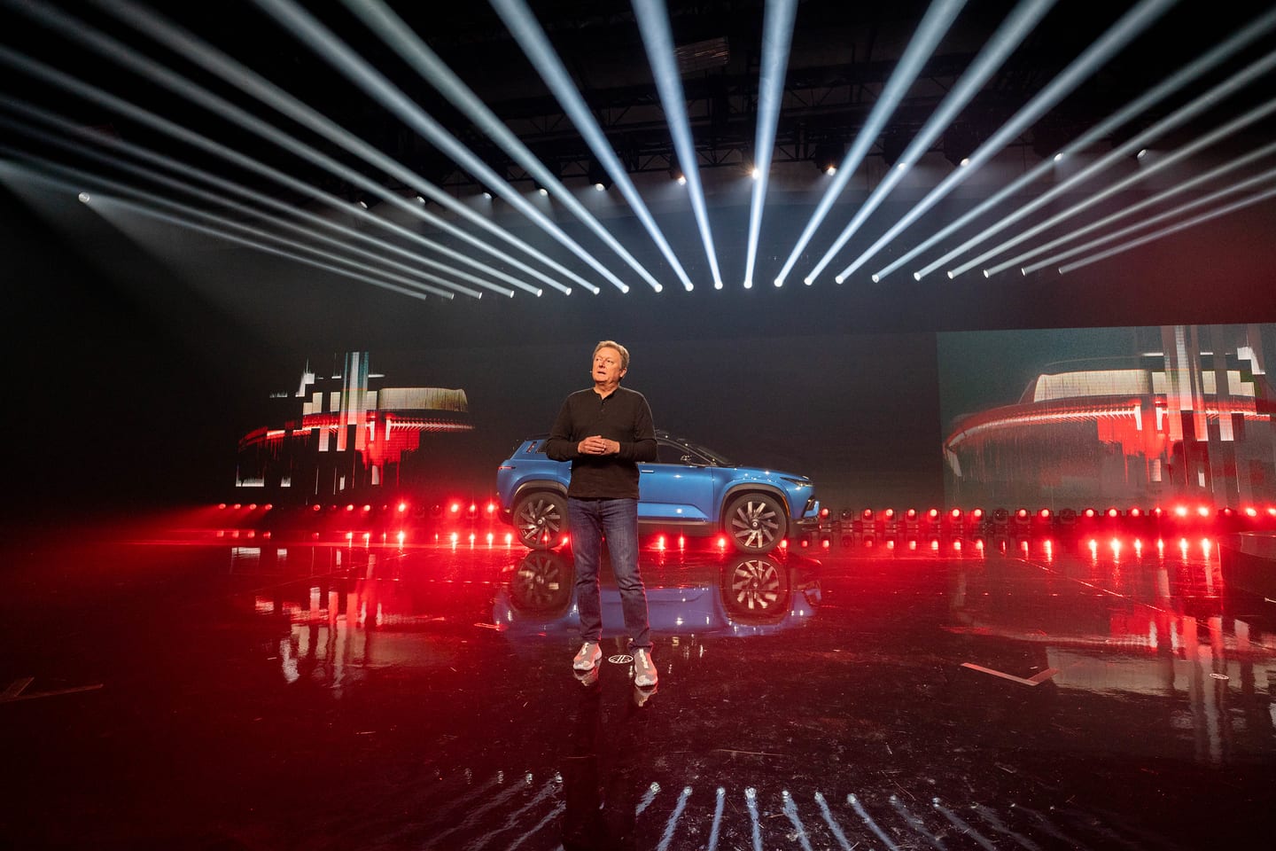 Wide view of a presenter beside a blue Fisker SUV on the reflective reveal stage