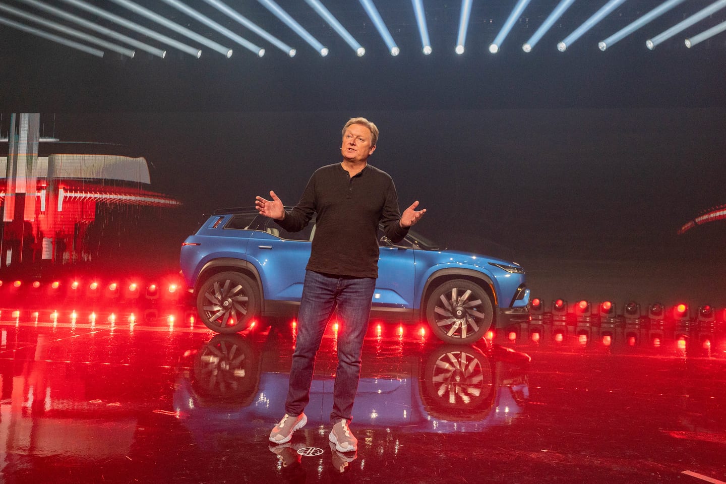 A presenter beside a blue Fisker SUV above a line of red floor lights