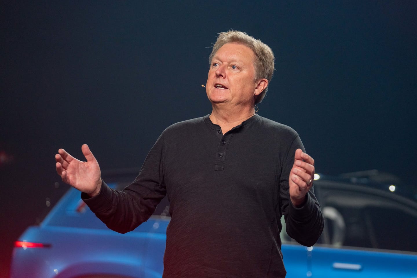 A presenter speaking on stage beside a Fisker vehicle