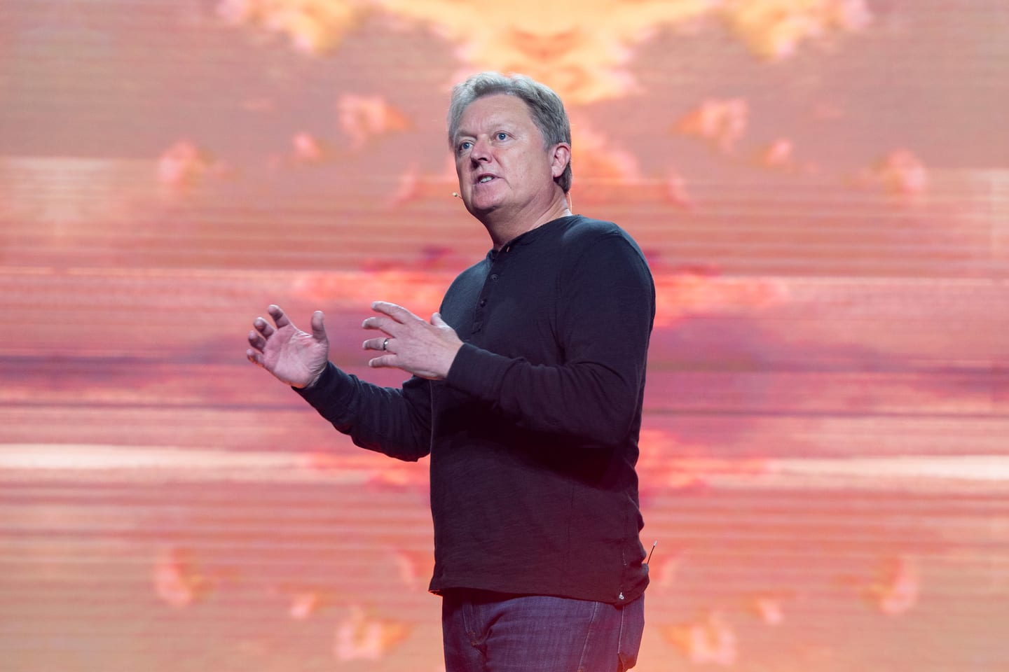 A presenter speaking in front of a wide orange landscape screen