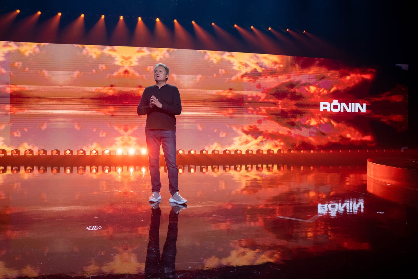 A presenter alone on stage in front of a wide RONIN screen