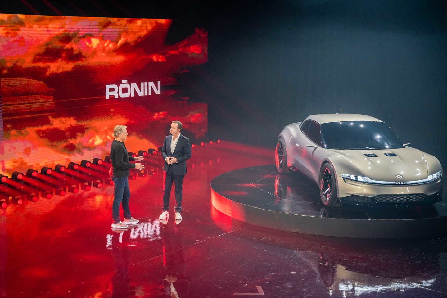 Two presenters on stage beside the Ronin against a red screen