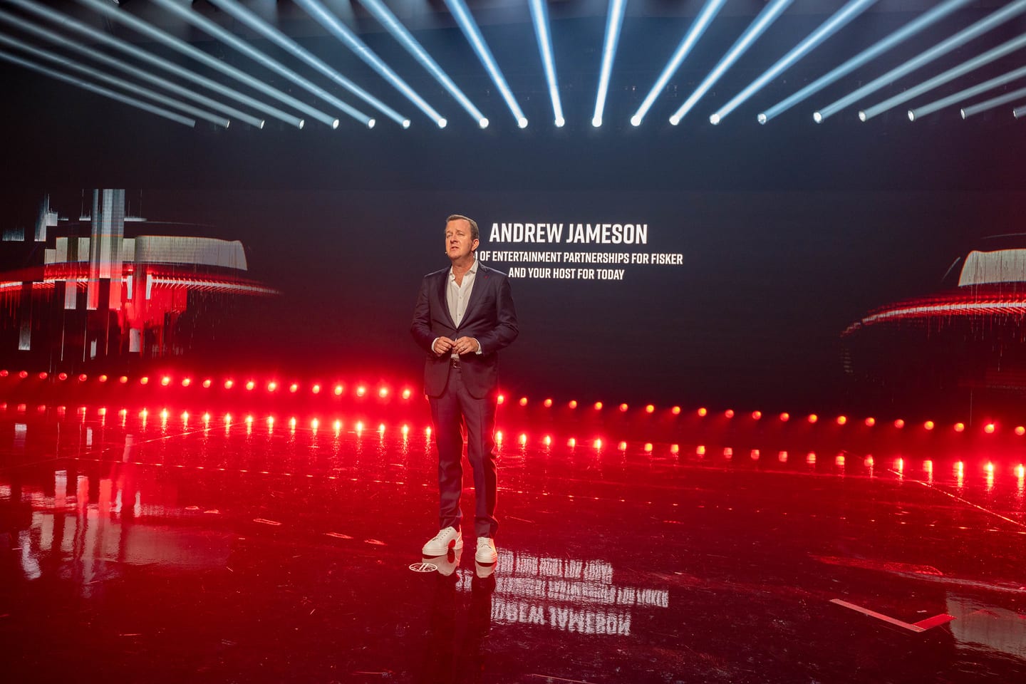 A speaker on stage with his name and title on the screen behind him