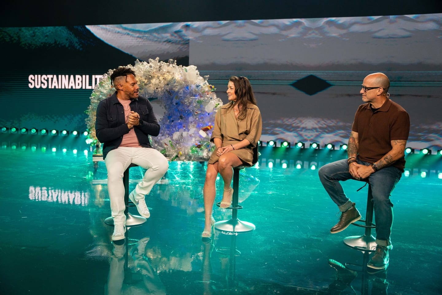 Panelists discussing sustainability on a teal-lit stage at a Fisker brand event