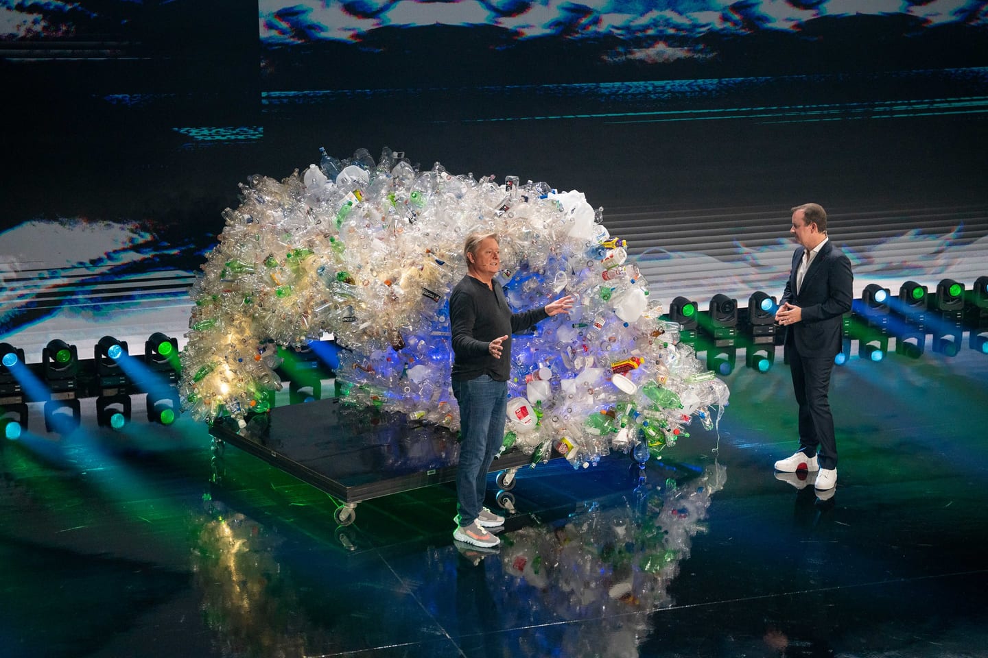A speaker on stage beside a sculpture made from recycled plastic