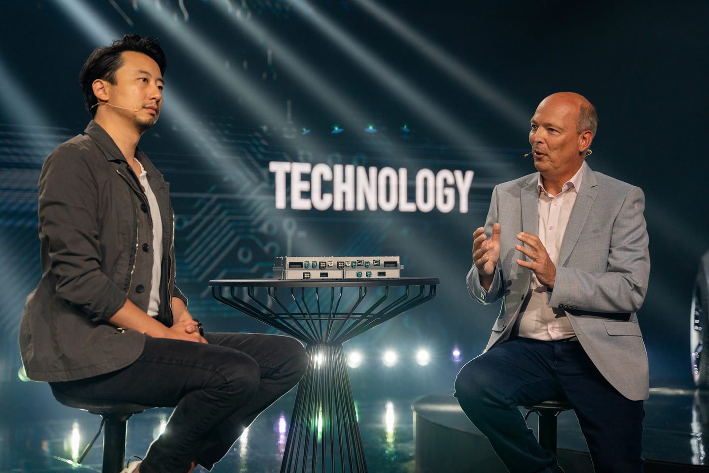 Two speakers in a fireside chat on stage in front of a screen reading TECHNOLOGY
