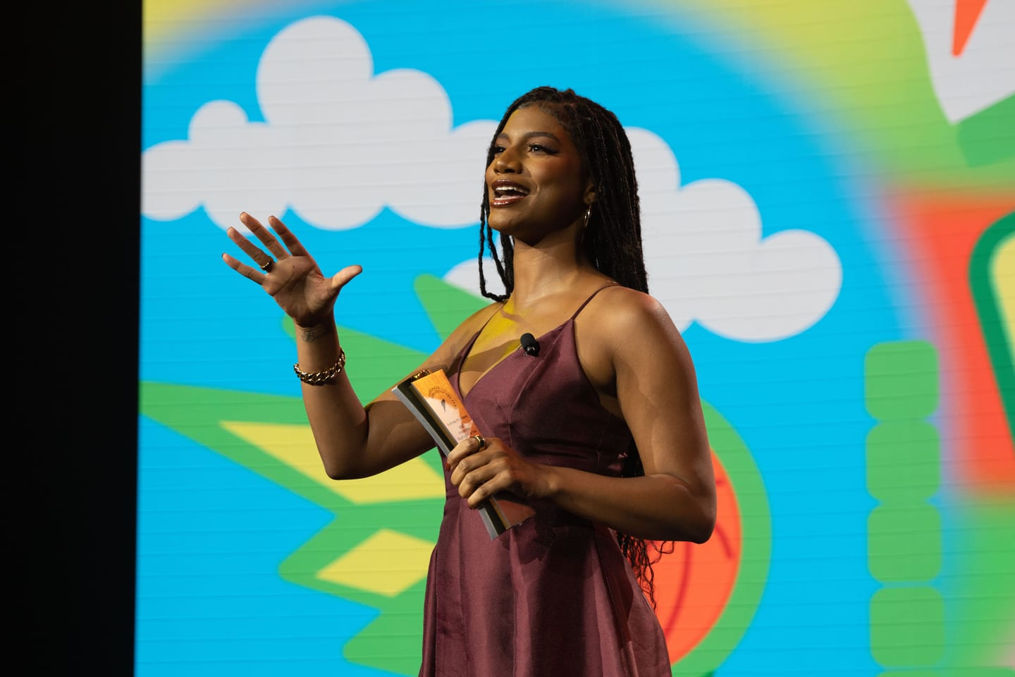 An award winner on stage holding her trophy in front of a bright illustrated backdrop