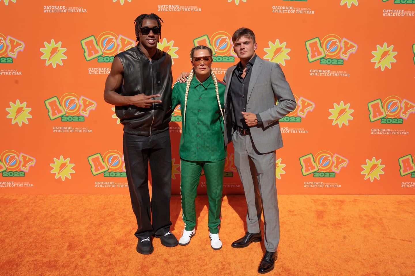 A group of guests posing with a host in a green Gatorade tracksuit on the orange carpet