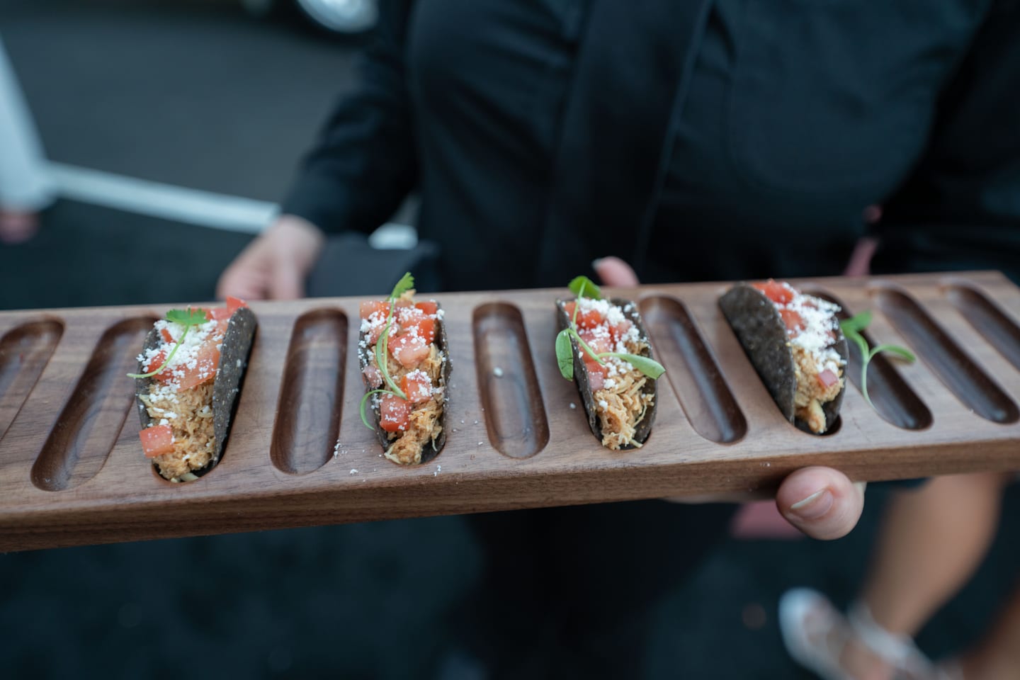 A server carrying a wooden tray of small plated bites through the reception