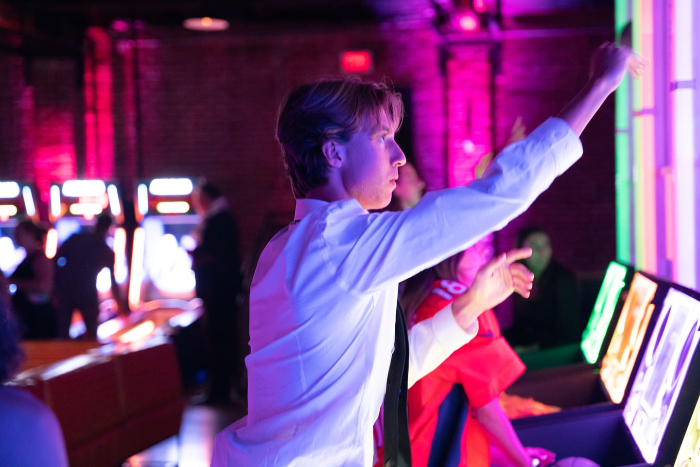 A guest playing an arcade cabinet in pink and blue light at the after-party