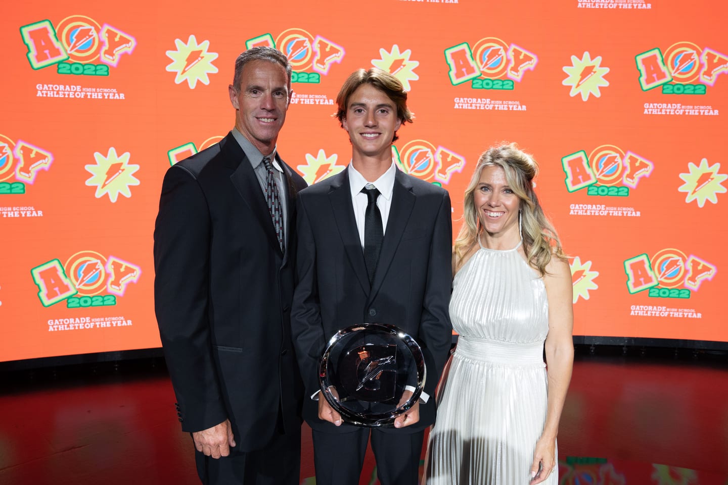 An Athlete of the Year honoree holding his trophy on the orange carpet between two guests