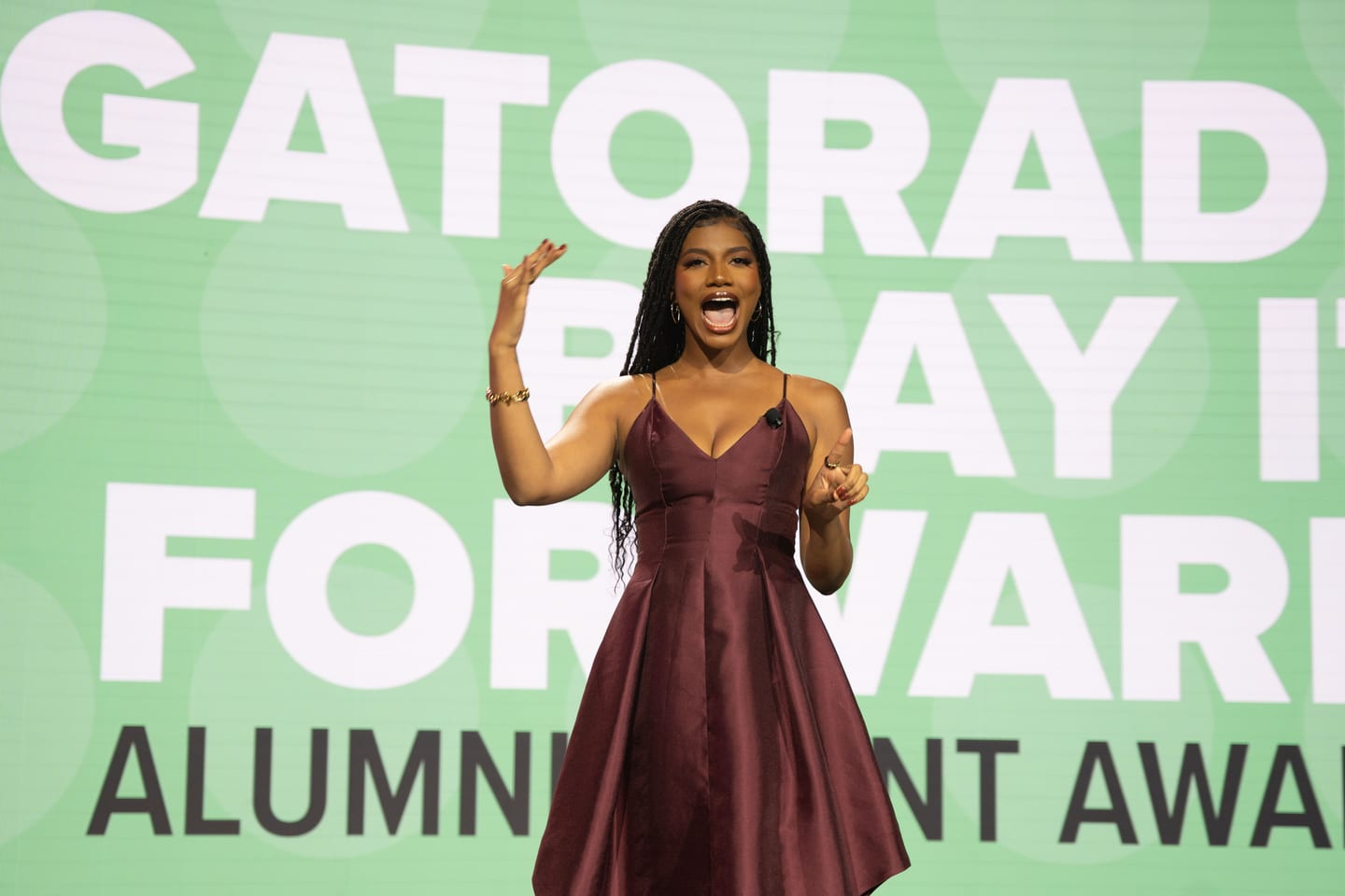 A speaker on stage in front of a screen reading Gatorade Play It Forward Alumni Award