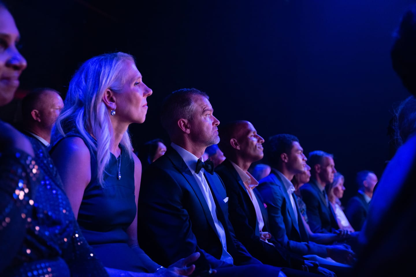 A row of guests seated in blue stage light during the ceremony