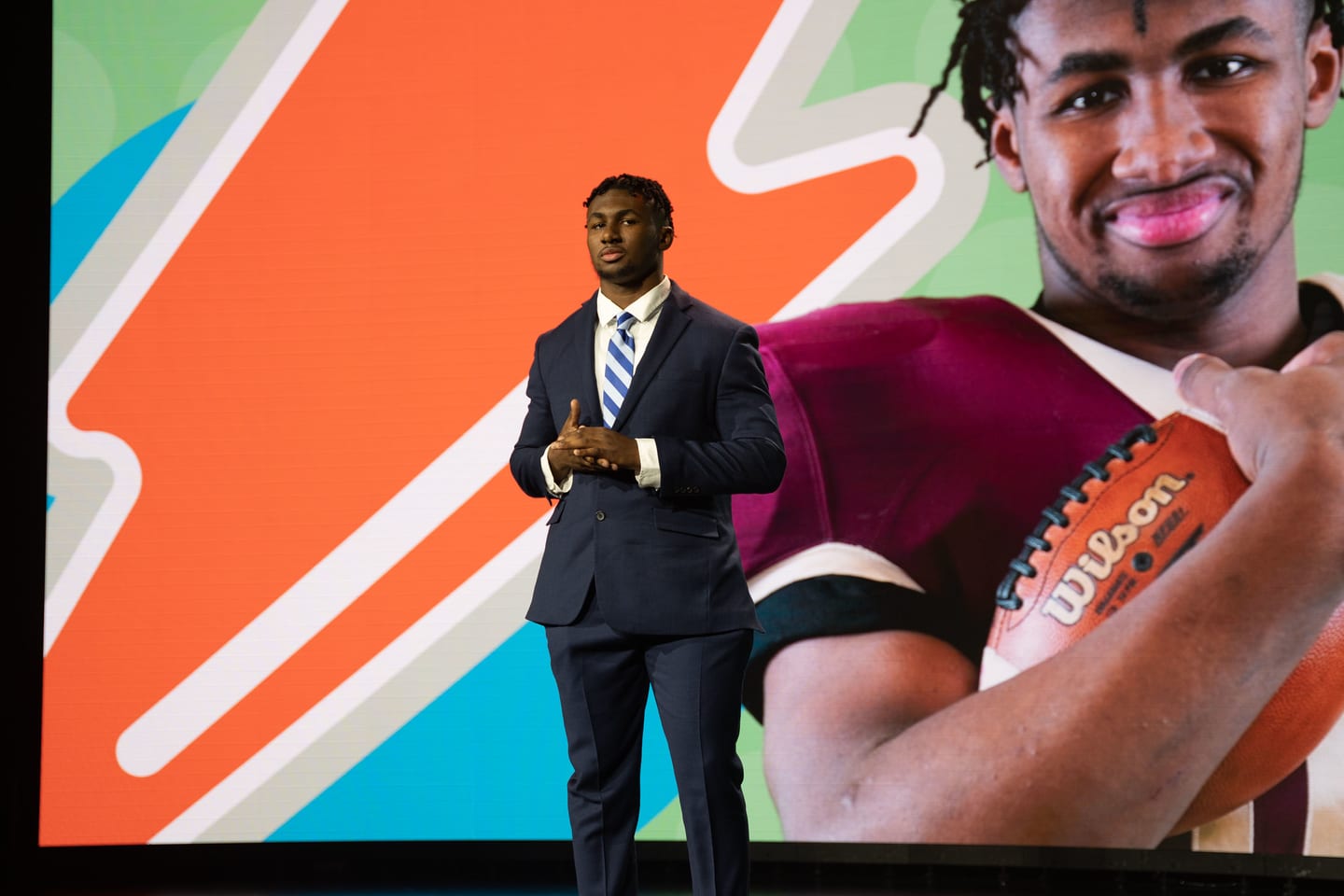 An honoree in a suit on the orange carpet in front of an oversized Wilson football graphic