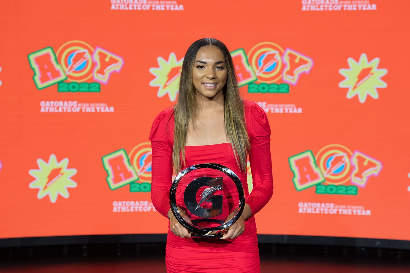 An honoree in red holding the Gatorade trophy on the orange carpet