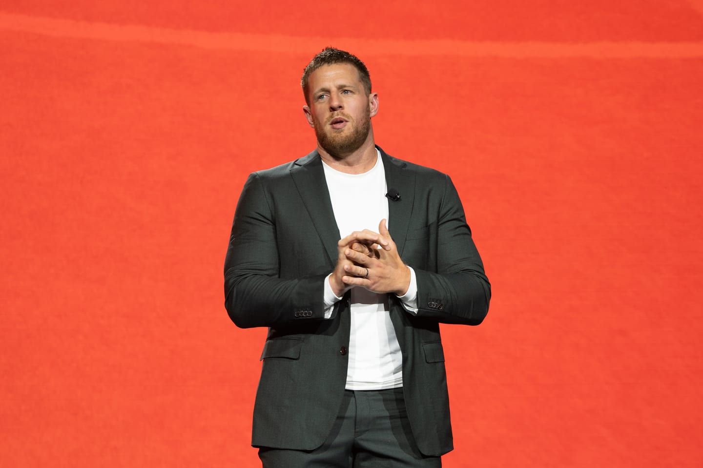 A presenter speaking on stage against an orange background