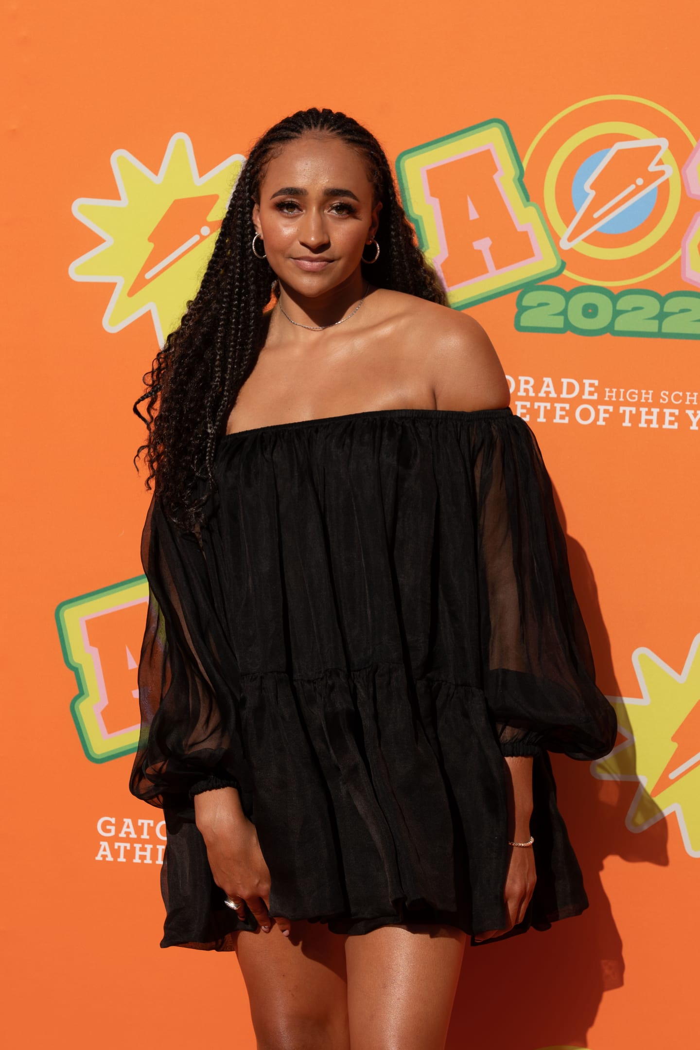 An honoree in a black dress photographed on the orange AOY 2022 step-and-repeat