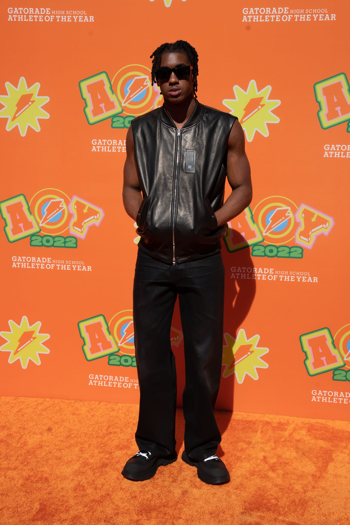 A guest in a leather jacket and sunglasses photographed on the orange AOY 2022 step-and-repeat