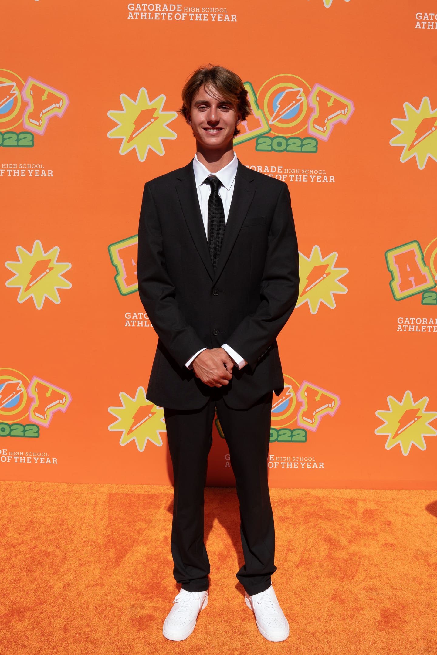An honoree in a black suit photographed on the orange AOY 2022 step-and-repeat