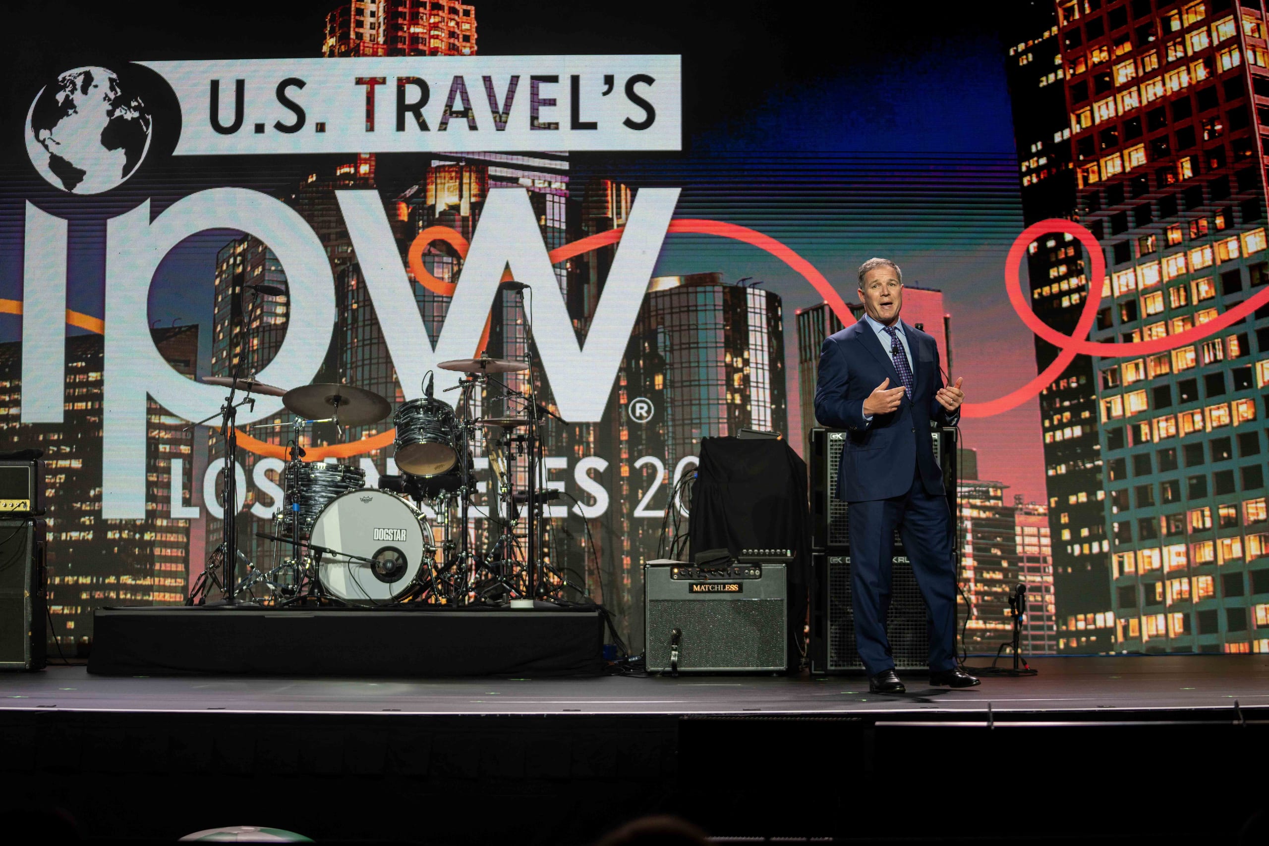 U.S. Travel Association president Geoff Freeman speaking on the IPW main stage before a large IPW Los Angeles 2024 city-skyline screen