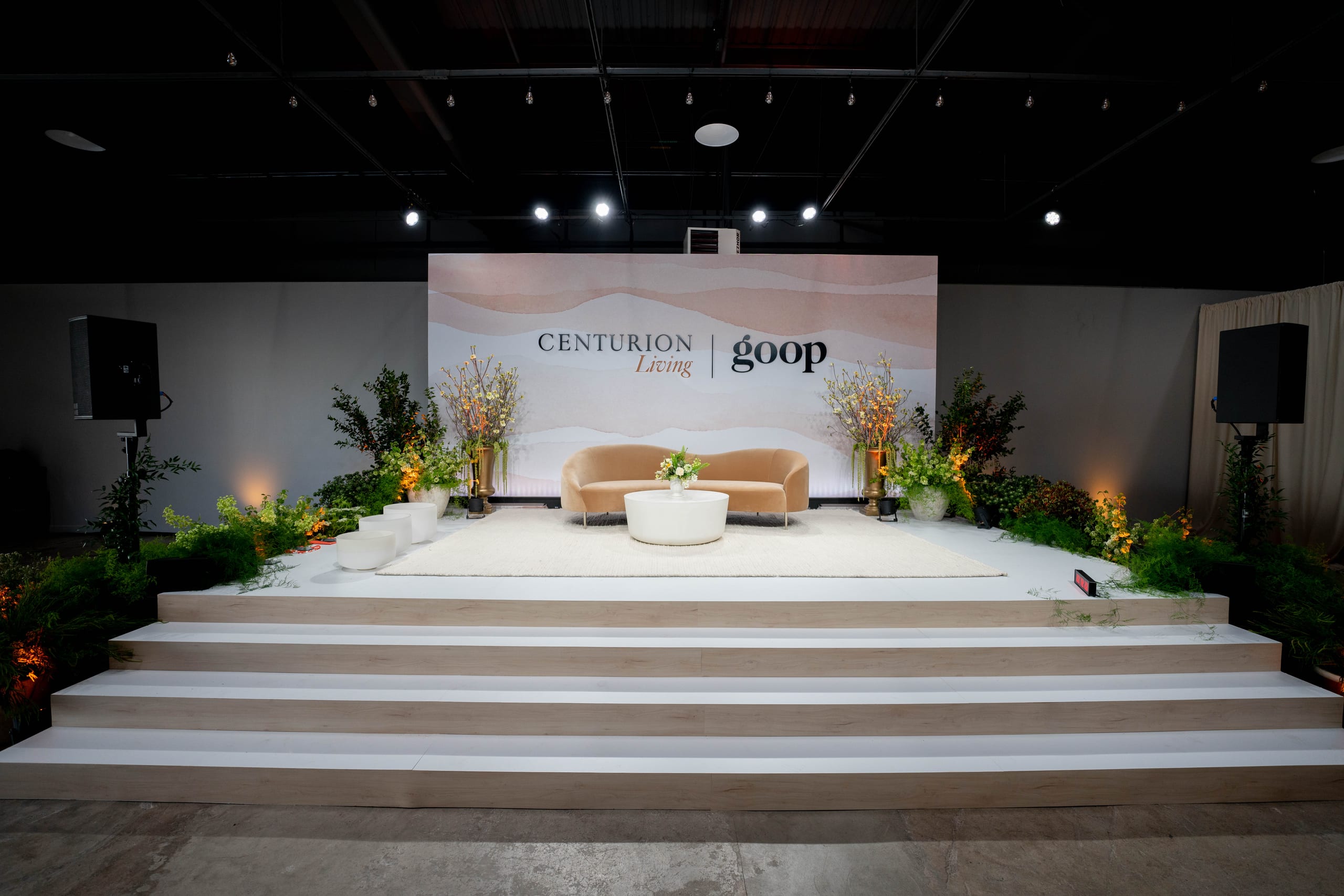 An empty branded stage set with a curved sofa, floral arrangements and a printed backdrop, photographed before guests arrived at a Los Angeles corporate brand event