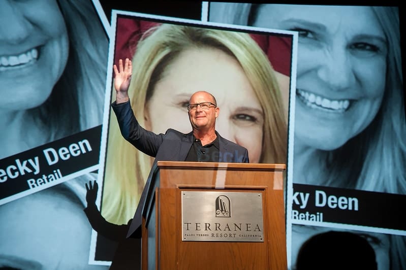 A speaker at a podium before large screens at a corporate health conference