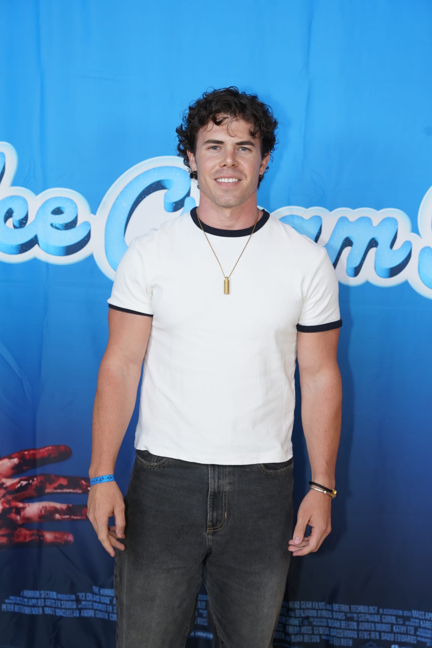A guest in a white ringer t-shirt posing against the blue Ice Cream Man branded backdrop at AMC The Americana at Brand