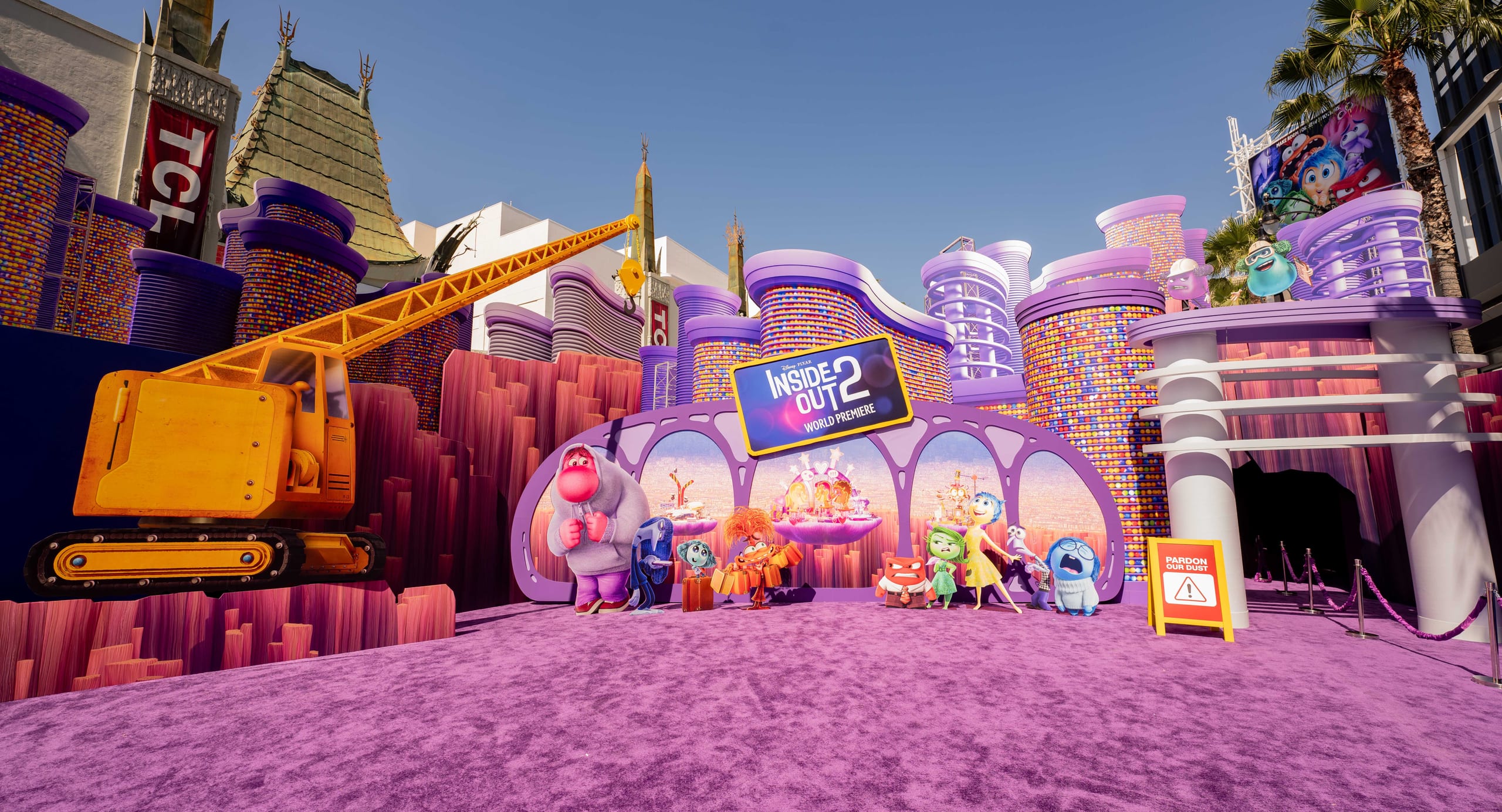 The Inside Out 2 world premiere carpet built out in front of the TCL Chinese Theatre before guests arrive — a purple carpet running up to an archway of character standees, towers of coloured memory orbs, a prop construction crane and a Pardon Our Dust sign under a clear blue sky