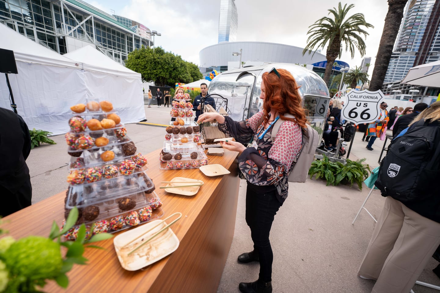 A guest picking from a donut tower beside an Airstream trailer and a California Route 66 sign at an outdoor IPW activation