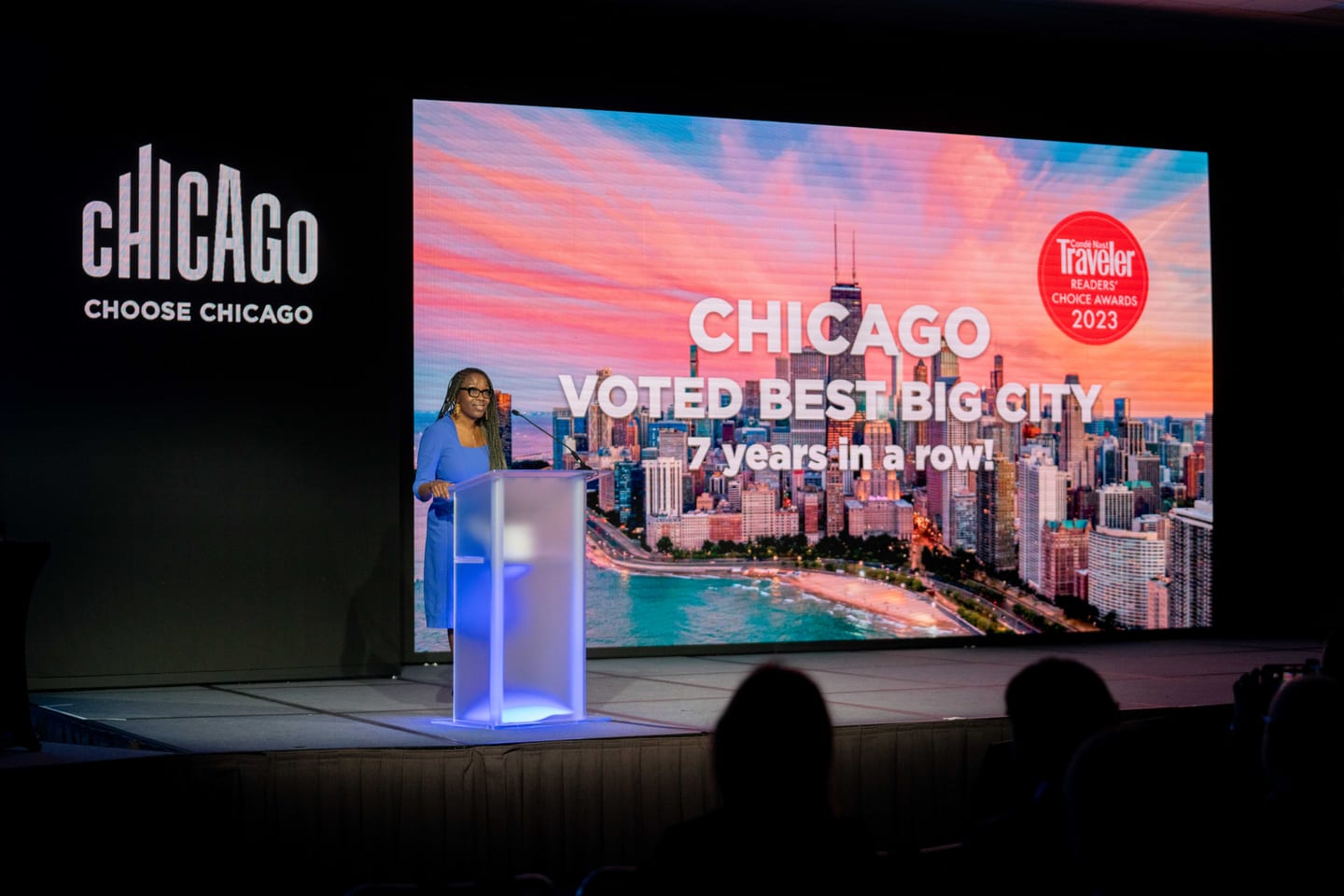 A speaker on the Choose Chicago stage beside a screen reading Chicago voted best big city seven years in a row at IPW