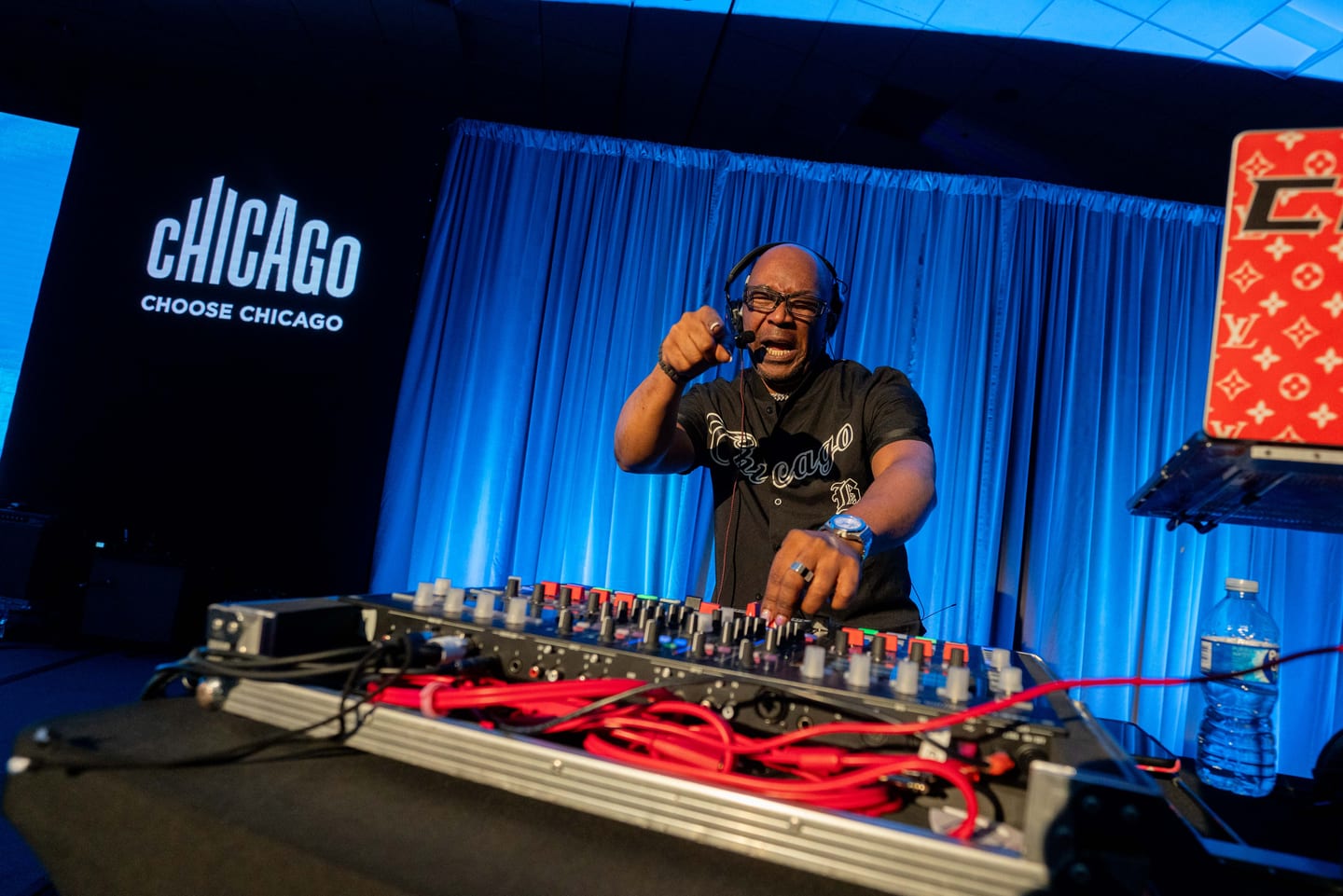 A DJ performing behind decks on a blue-lit stage at the Choose Chicago presentation at IPW