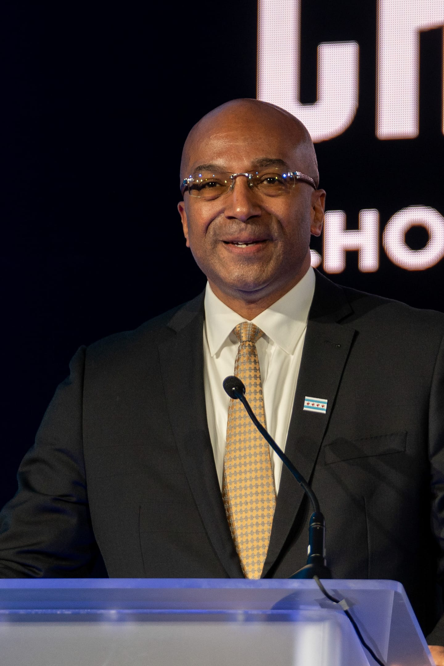 A speaker in a dark suit and gold tie at a podium in front of a Choose Chicago backdrop at IPW