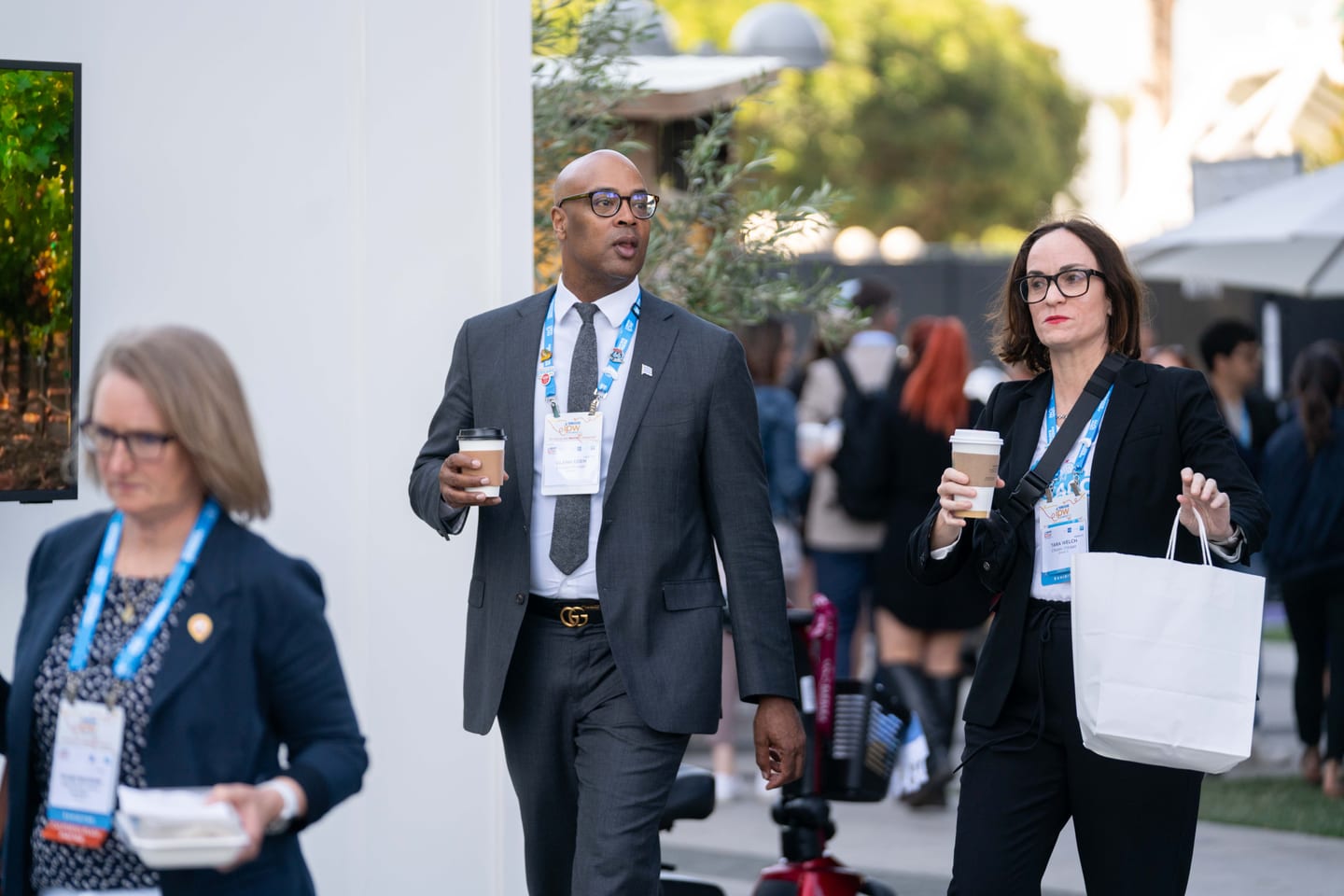 IPW delegates in suits and badges walking with coffee outside the Los Angeles Convention Center