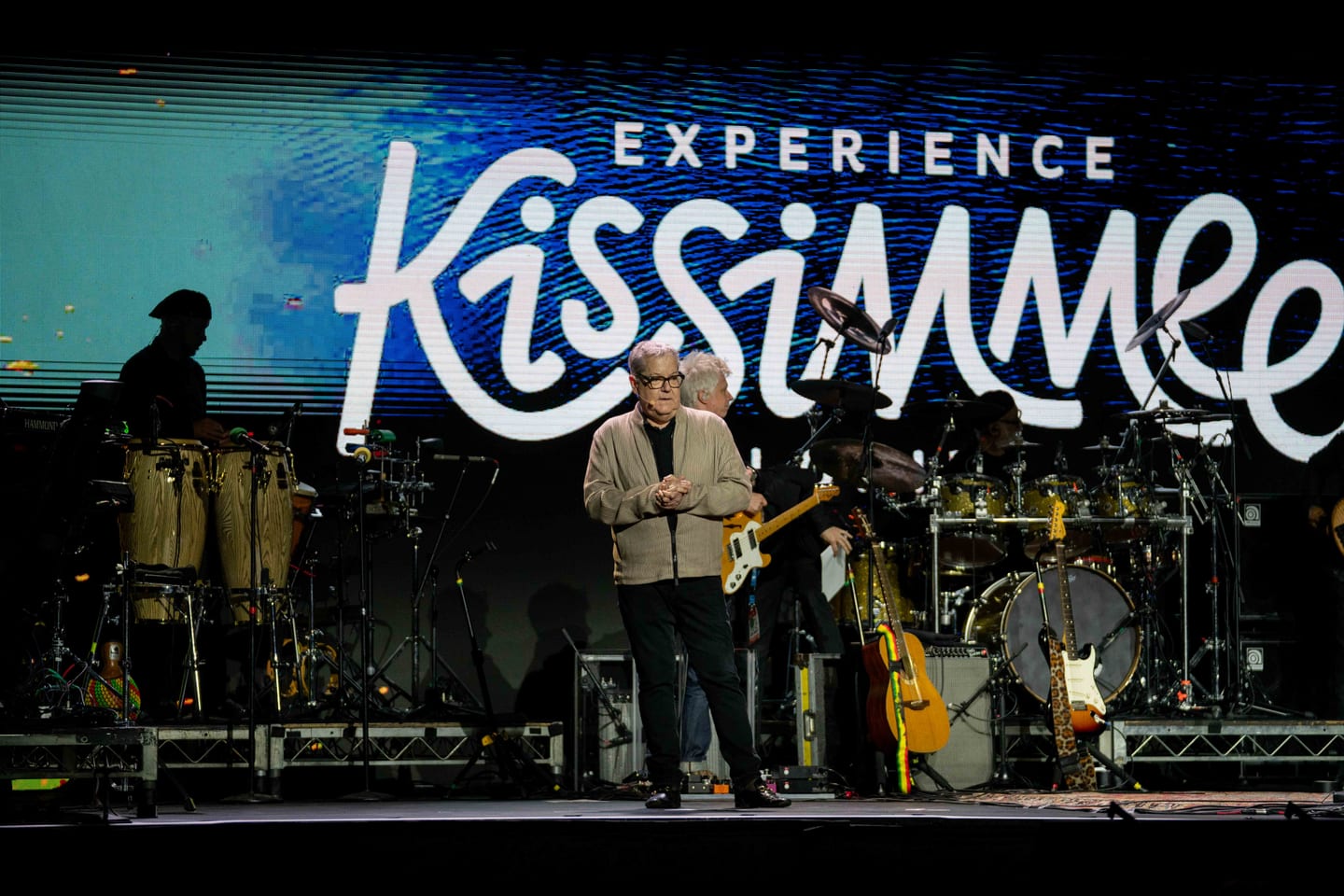 A band performing on a lit stage beneath a large Experience Kissimmee screen at IPW