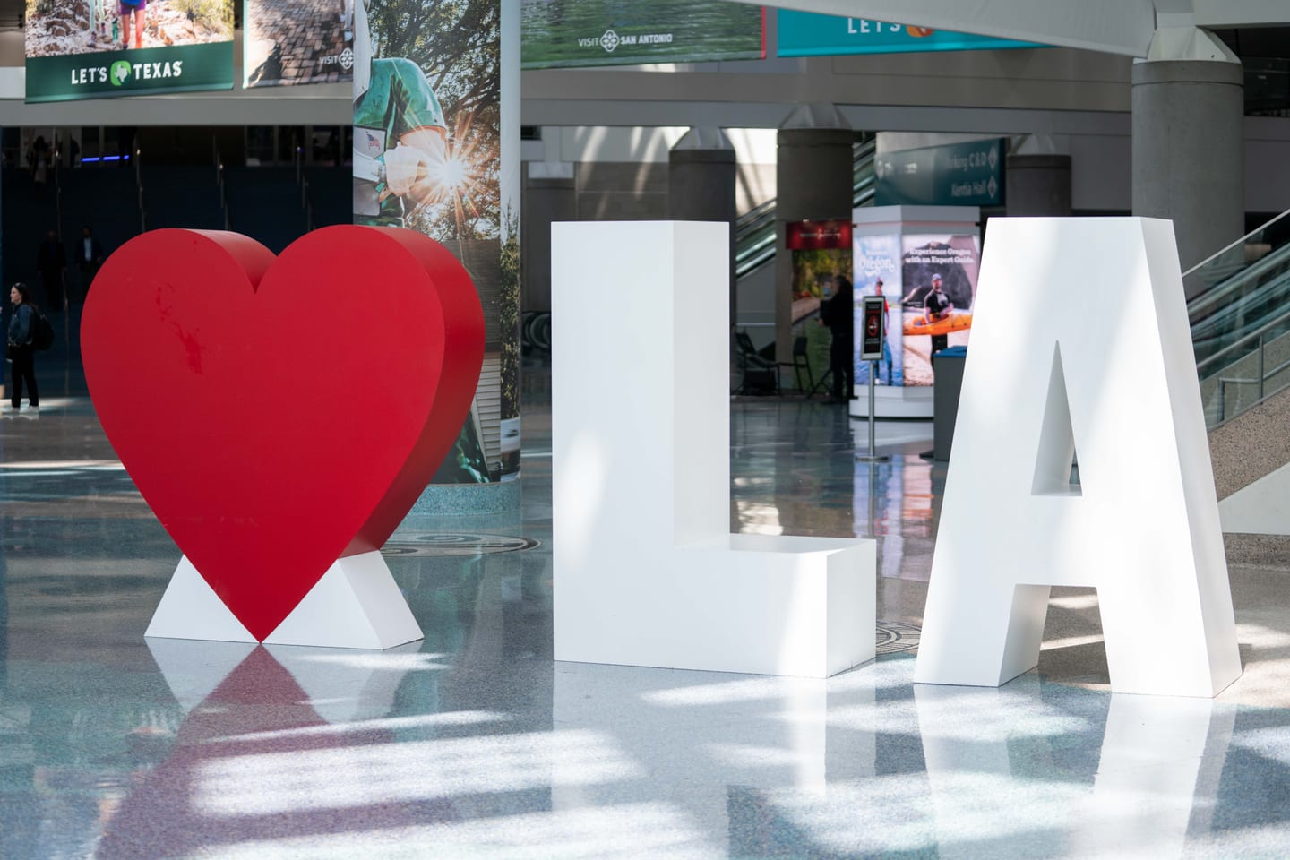Large white I heart LA letters standing in the Los Angeles Convention Center lobby beside destination banners at IPW