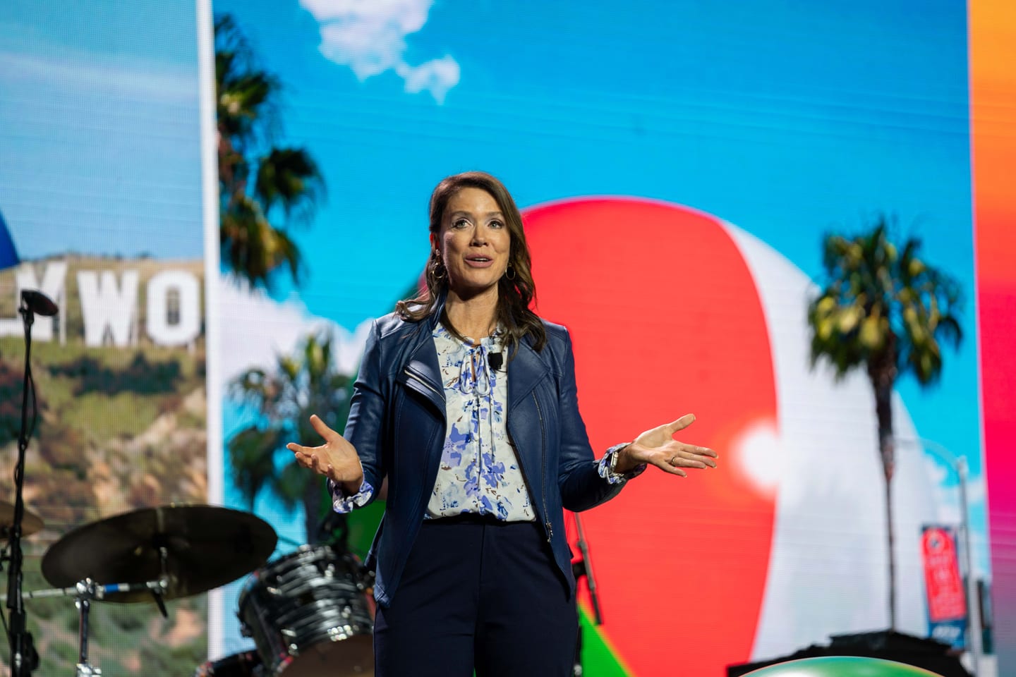 A speaker presenting on the IPW main stage in front of a wide screen showing the Hollywood sign and palm trees