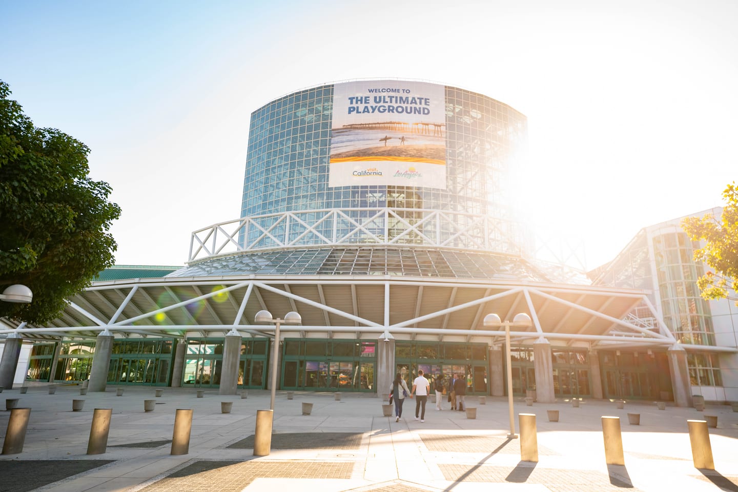 The glass entrance of the Los Angeles Convention Center at sunset under a Welcome to the Ultimate Playground banner during IPW