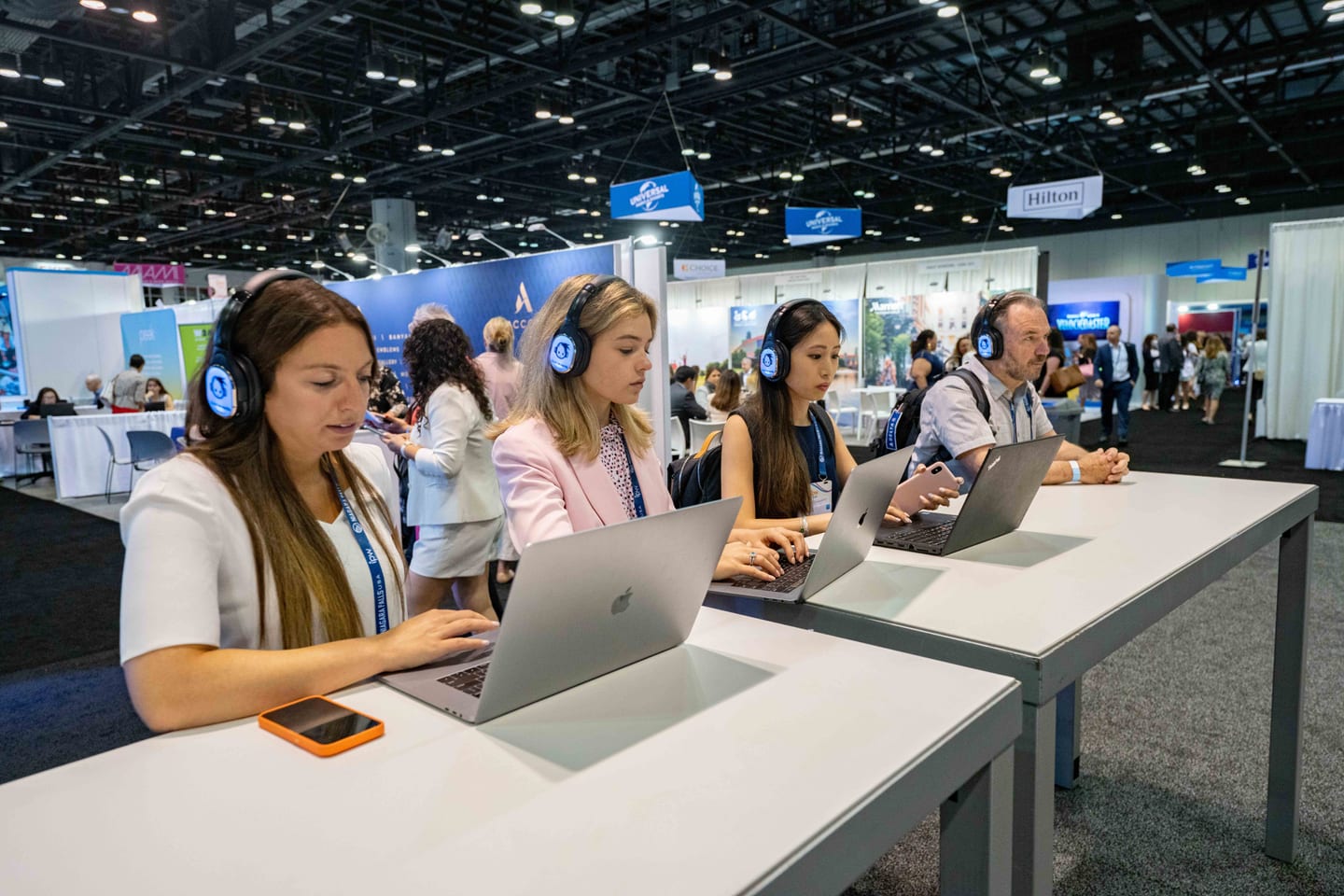 Attendees at laptops wearing headphones at listening stations on the IPW travel trade show floor